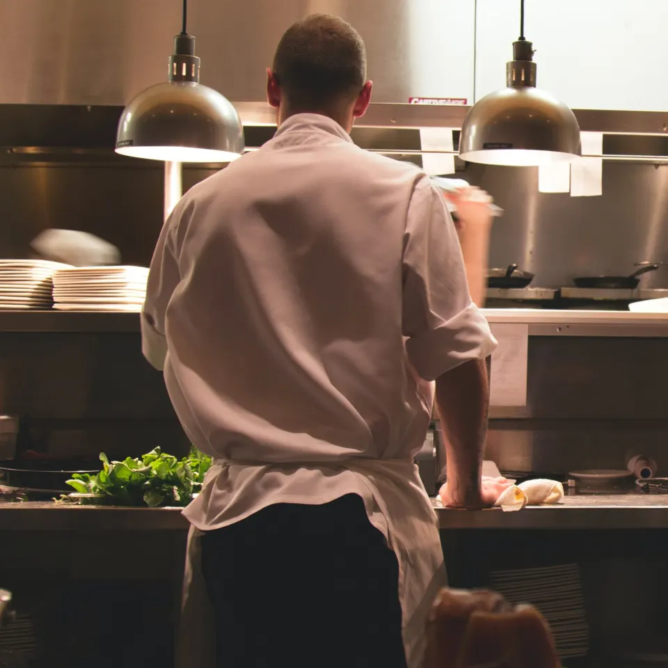 A chef in a white uniform cleaning the counter in a restaurant kitchen.