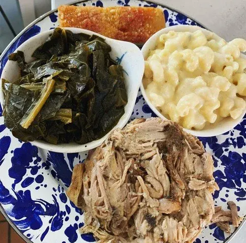 Plate of cooked collard greens, macaroni and cheese, pulled pork, and a piece of cornbread.