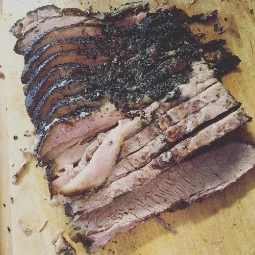 Sliced barbecue brisket with a dark seasoning crust on a wooden cutting board